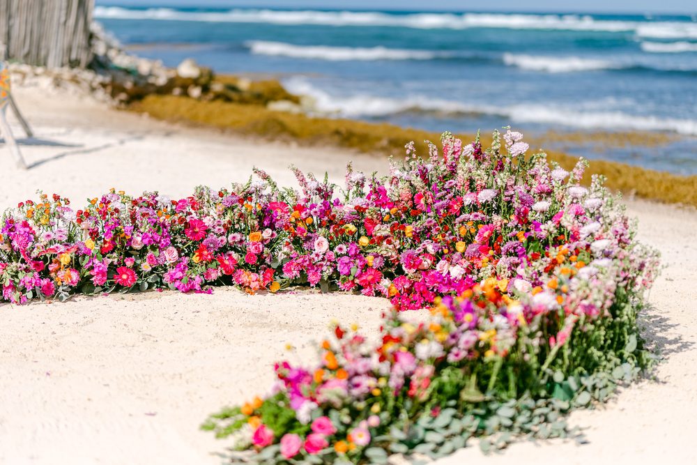 Arco floral rosa y naranja para la ceremonia sobre la arena, con el Caribe al fondo