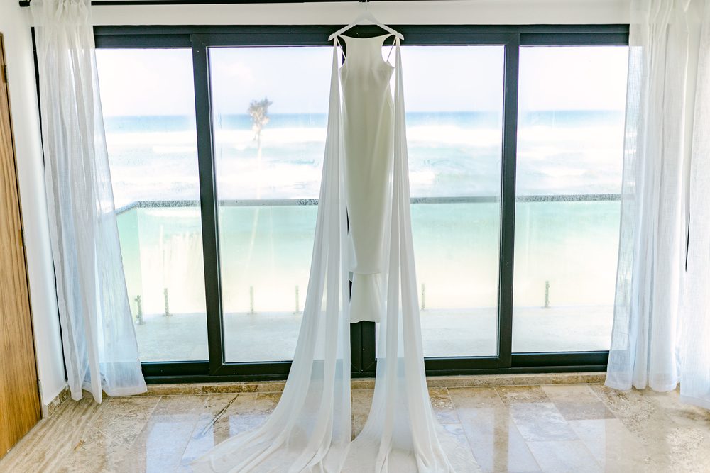 Vestido de novia colgado frente a una ventana con vista al mar